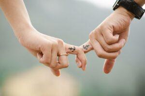 Twee handen waarvan de wijsvingers in elkaar haken. Op beide wijsvingers is een tattoo van een anker.